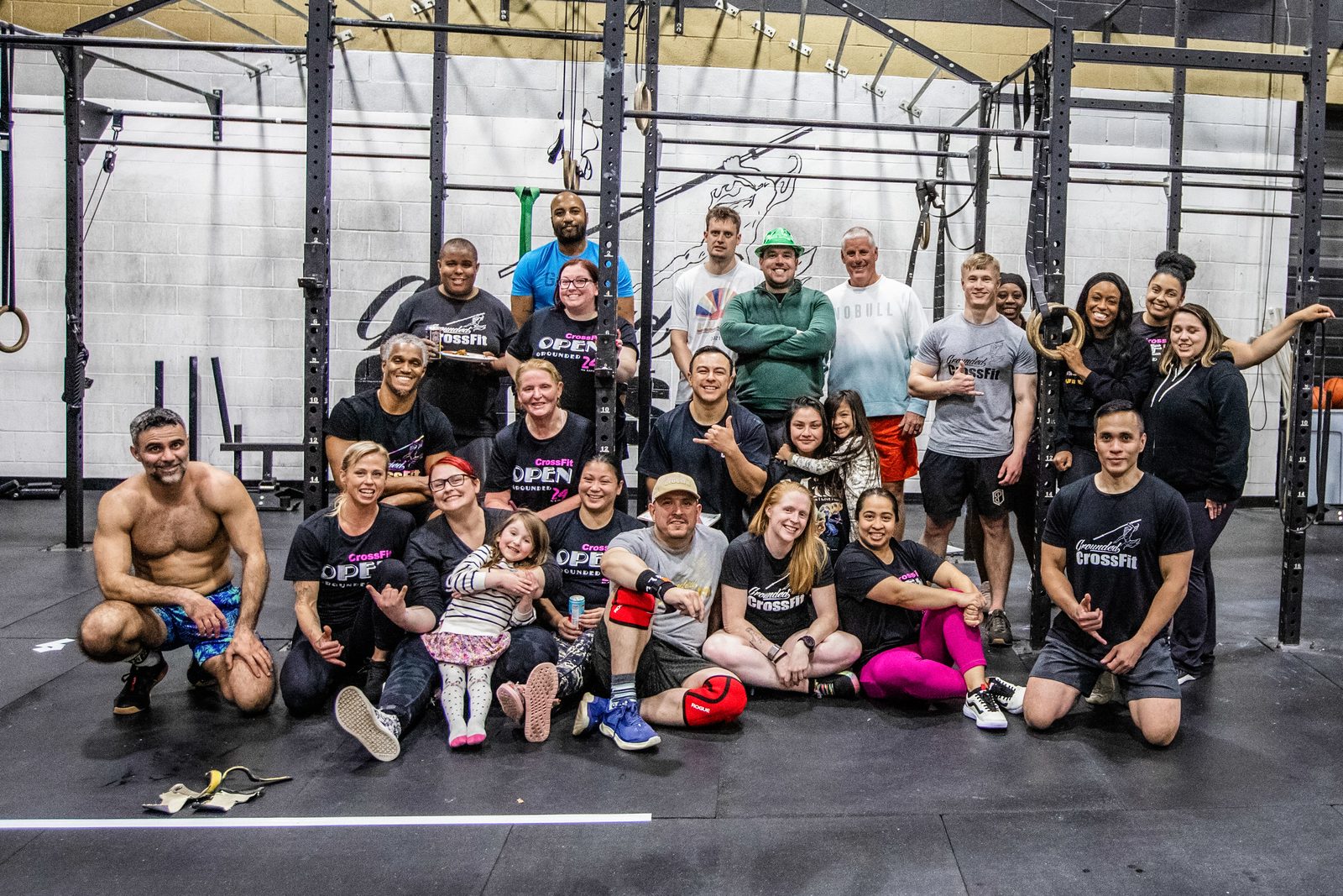 Grounded members and their kids gathered on the gym floor in CrossFit Open shirts